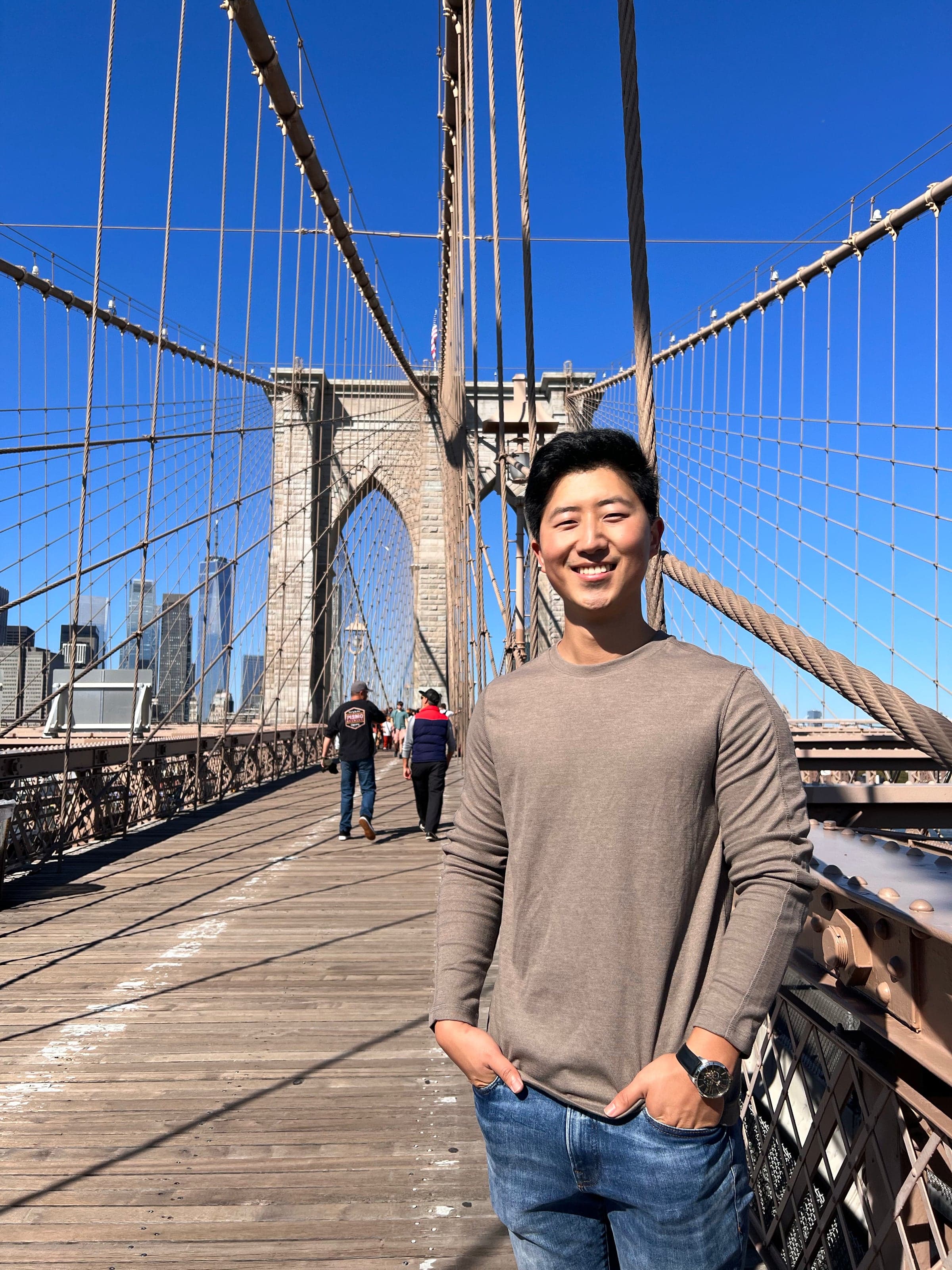Daniel Zhang, head of operations, on the Brooklyn Bridge walkway with the Manhattan skyline behind him.